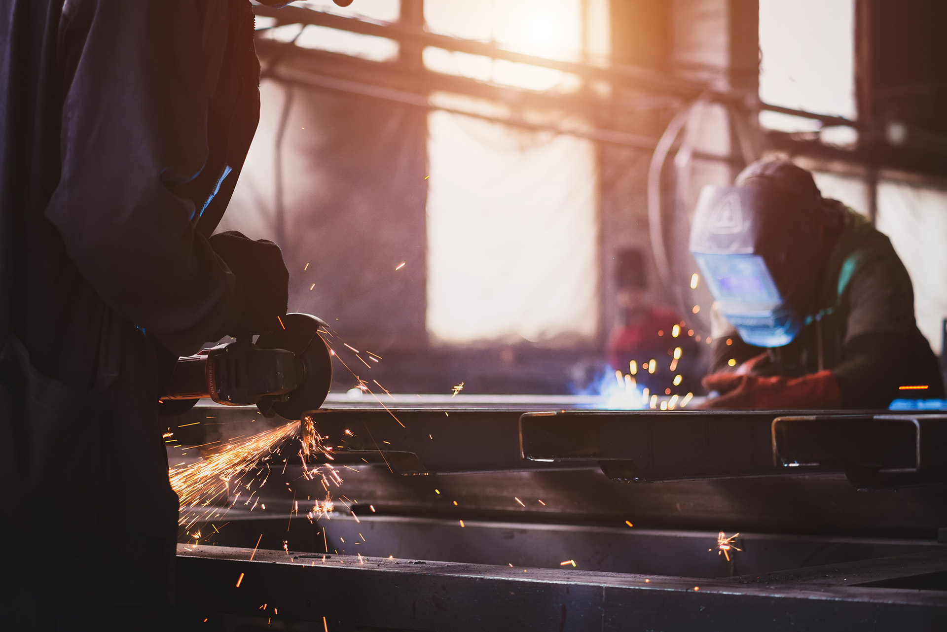 Two men cutting and welding steel in a fabrication shop