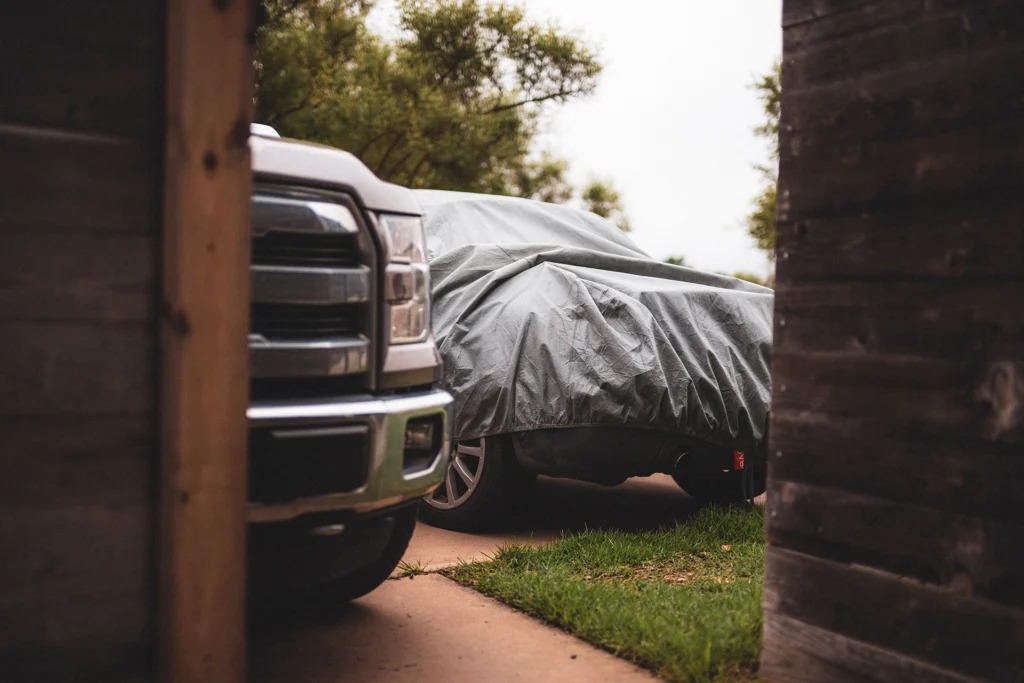 Two cars, one covered by a tarp, sit in a driveway
